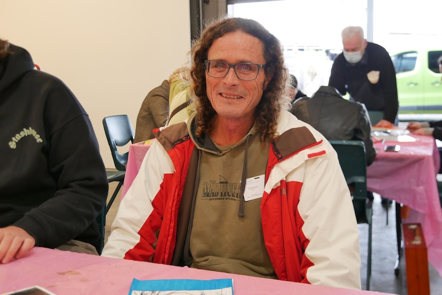 A man with long curly hair sits and smiles.