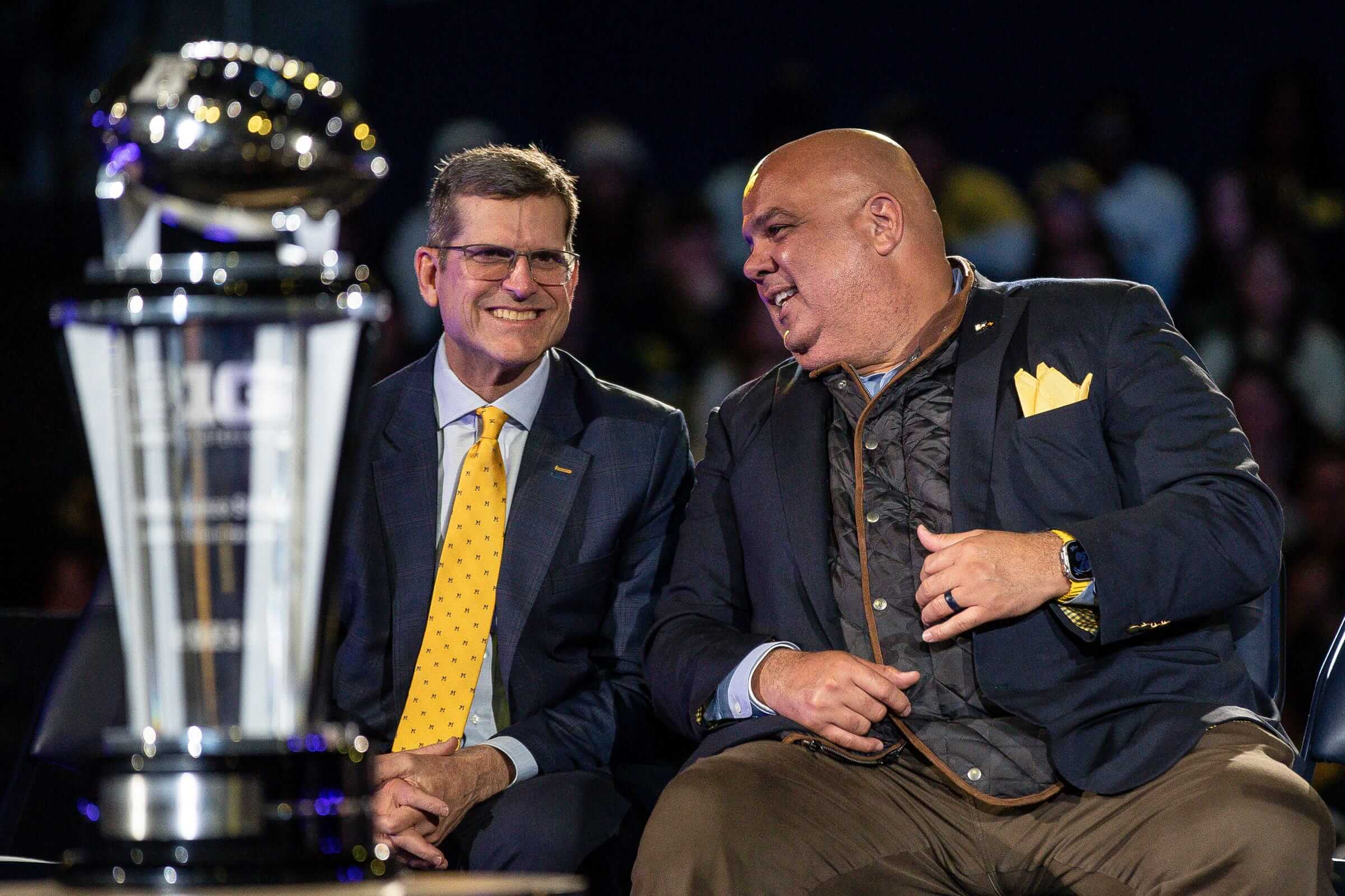 Warde Manuel leans to his left and talks to Jim Harbaugh behind the Big Ten championship trophy