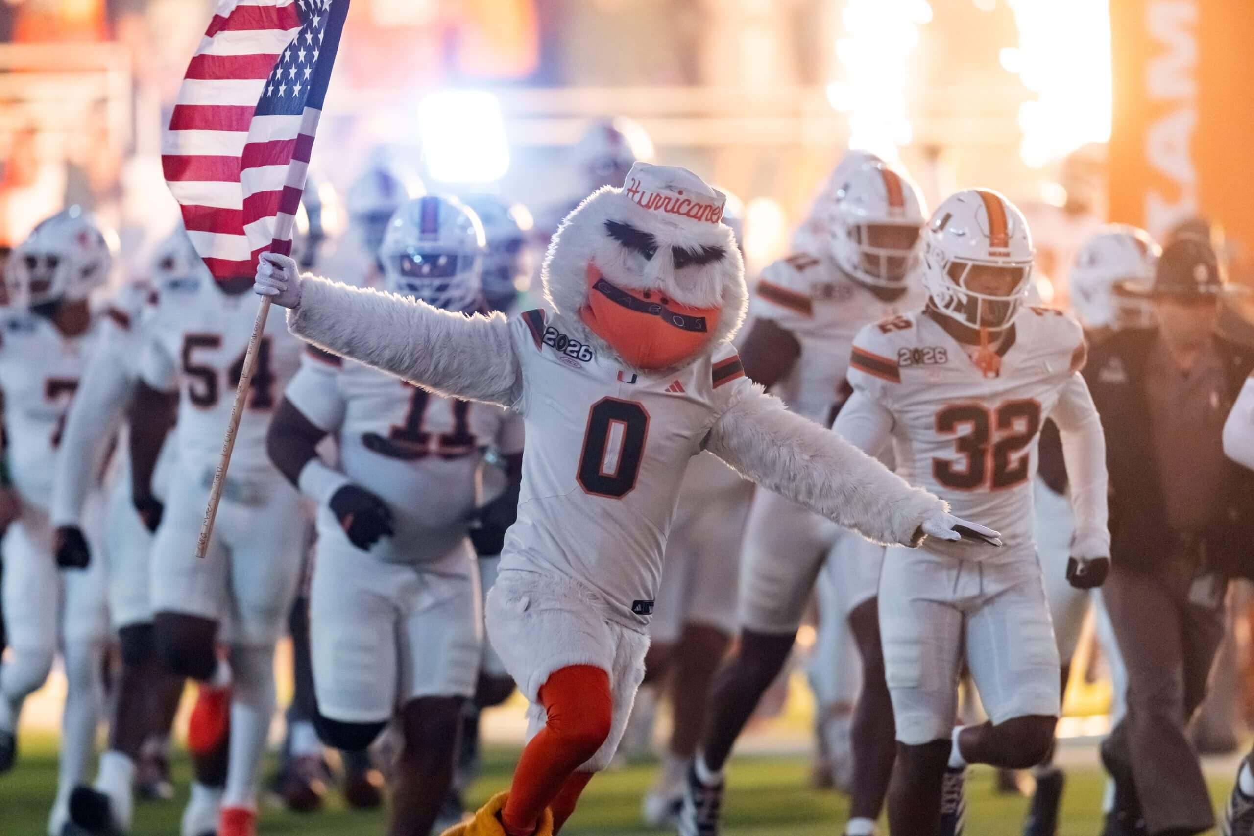 The Miami Hurricanes mascot runs on the field with the American flag in hand.