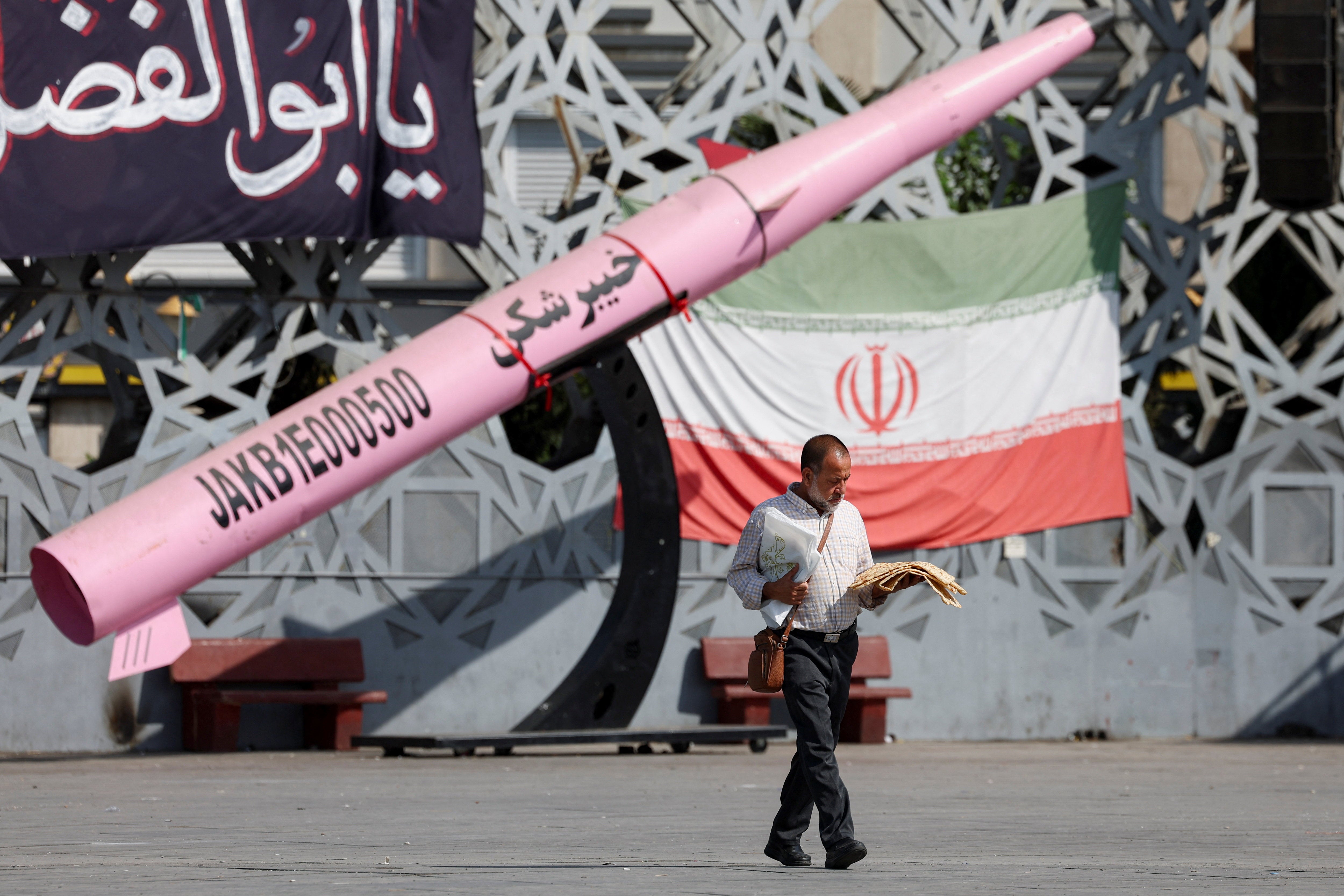 A man walks next to a symbolic mockup of an Iranian missile and an Iranian flag at Imam Hussein Square in Tehran, Iran