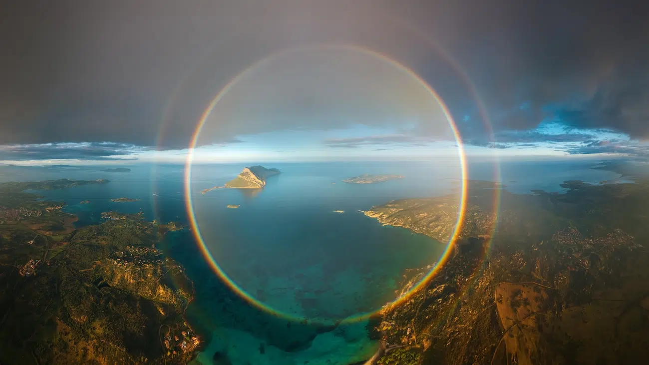 Complete rainbow in a perfect circle across a coastal landscape