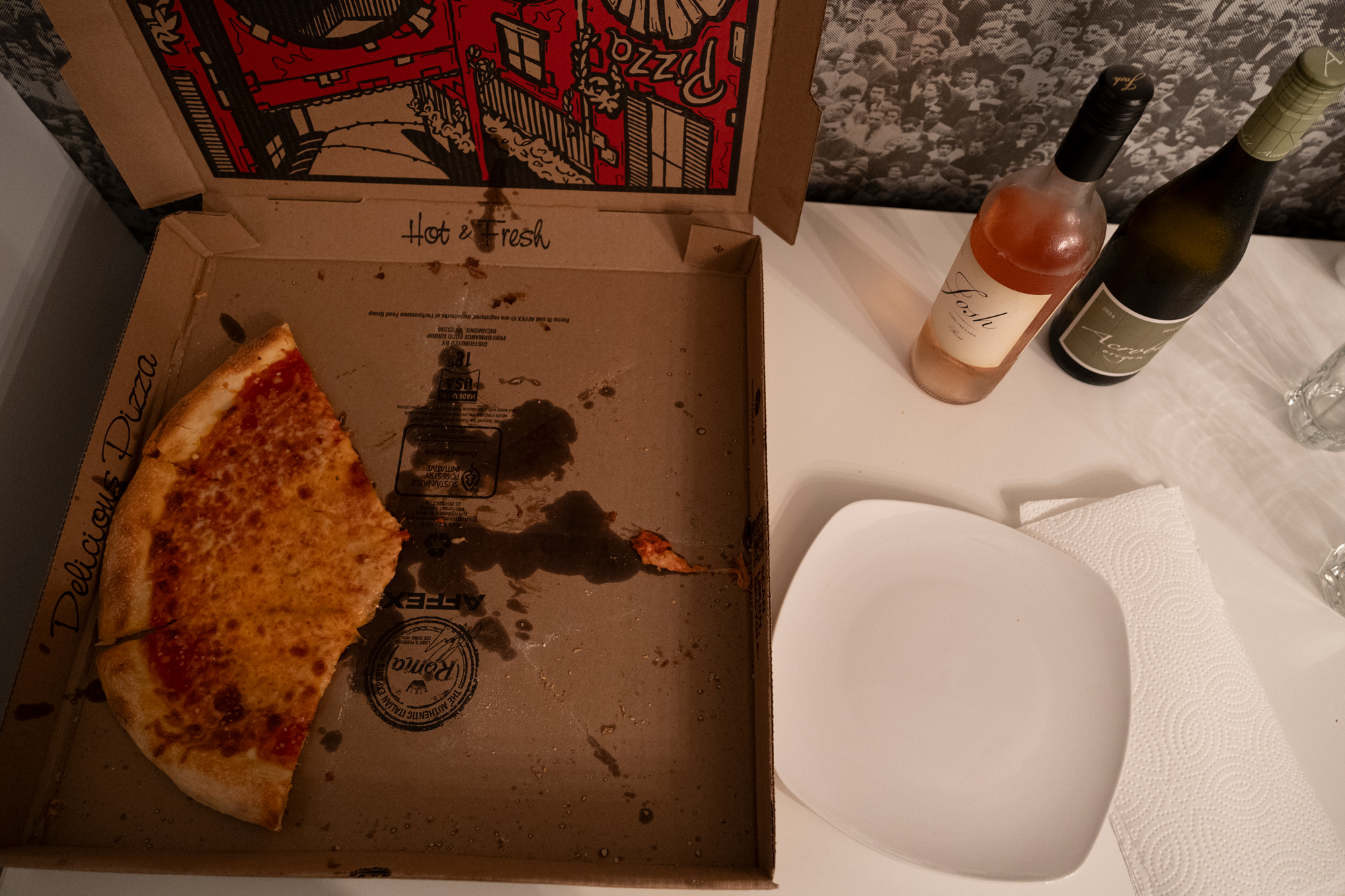 An open cardboard pizza box with three slices of cheese pizza beside bottles of rosé and pinot gris.