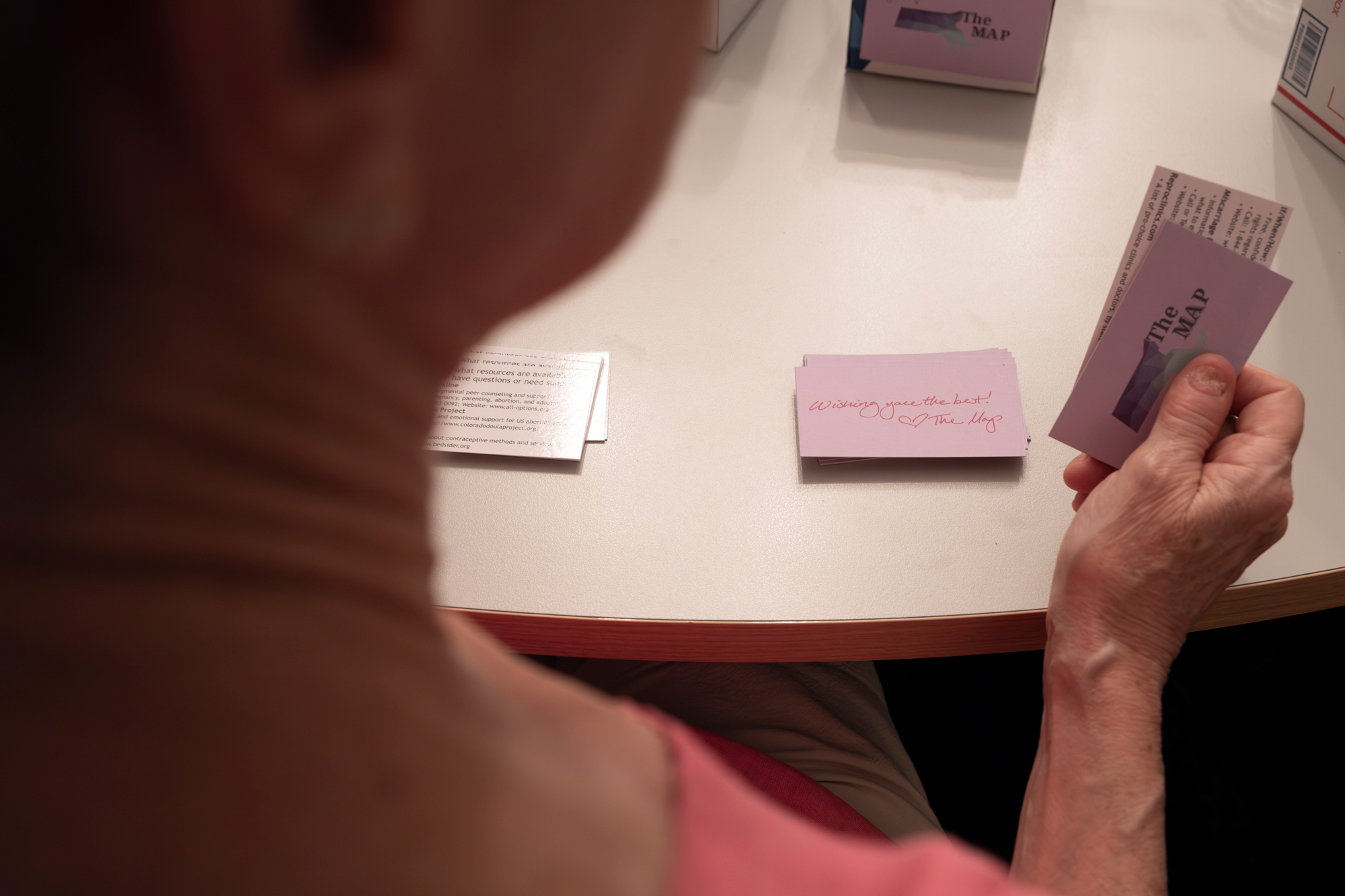 Seen over the shoulder of a volunteer, a handwritten purple note card reads, "Wishing you the best! [Heart drawing] The Map."