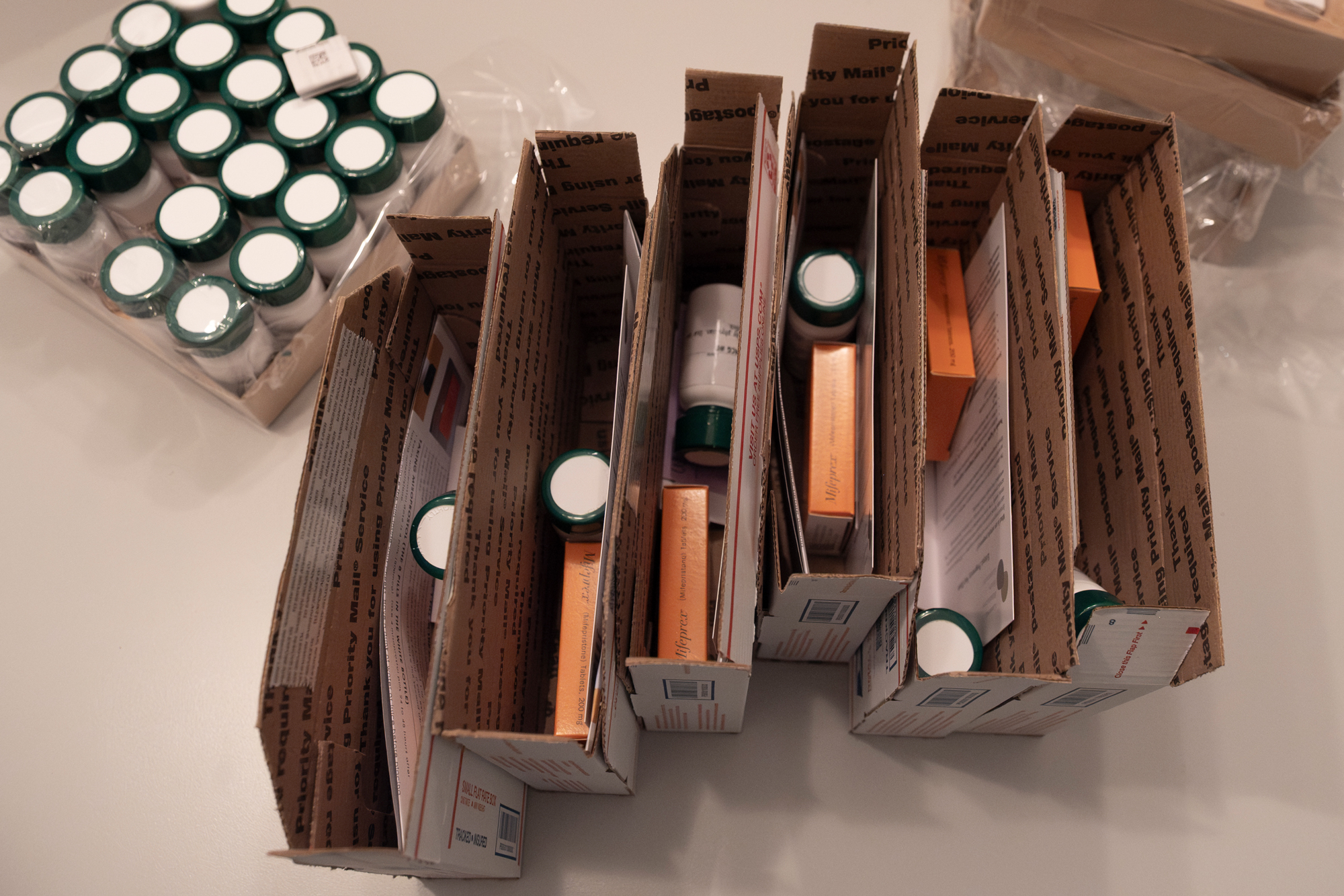 Slender USPS boxes, with their tops still unsealed, hold bottles and boxes of pills inside them.