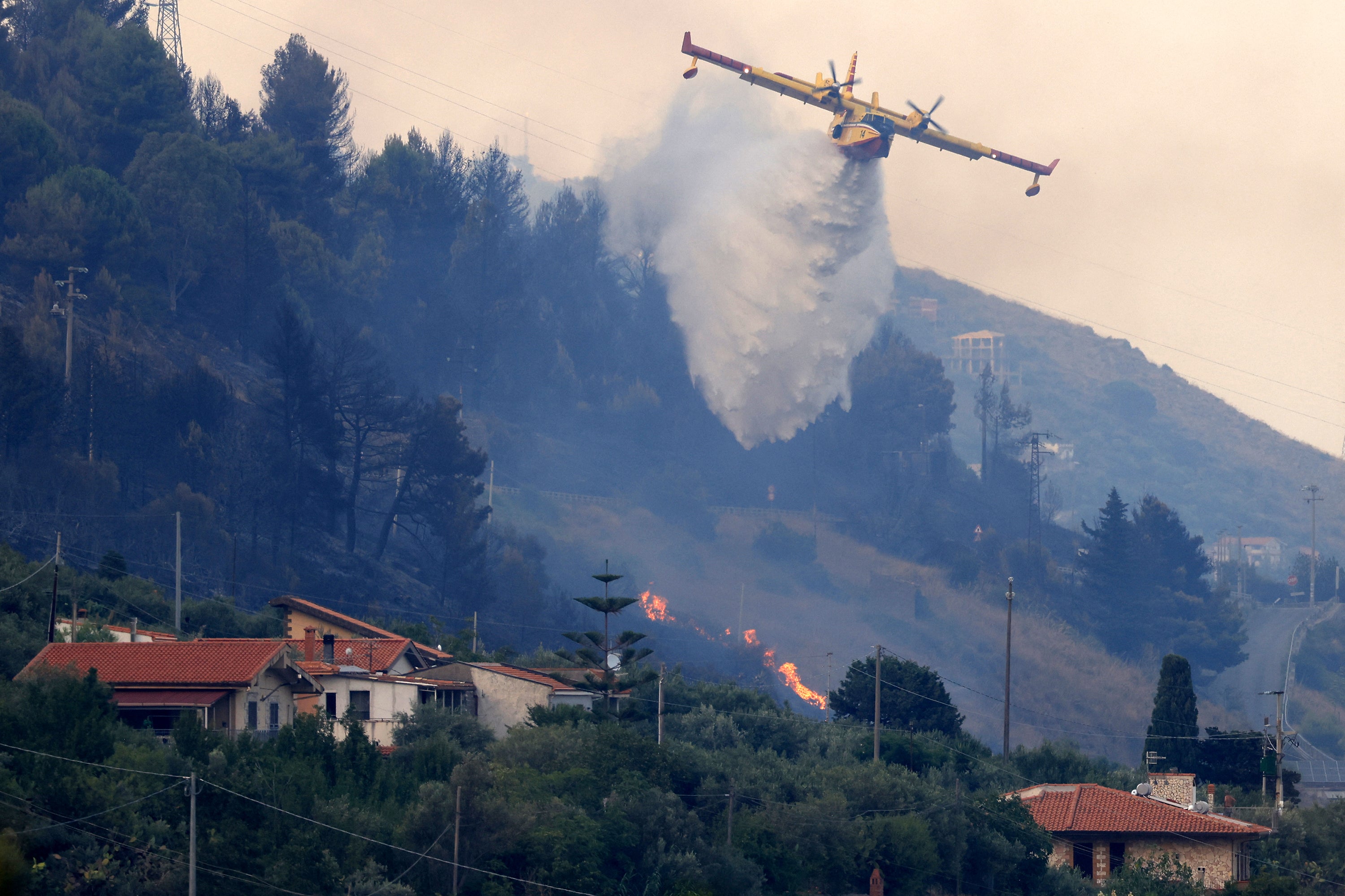 A Canadair drops water over a burning area as a wildfire flares in Sagana in the territory of Monreale, Sicily