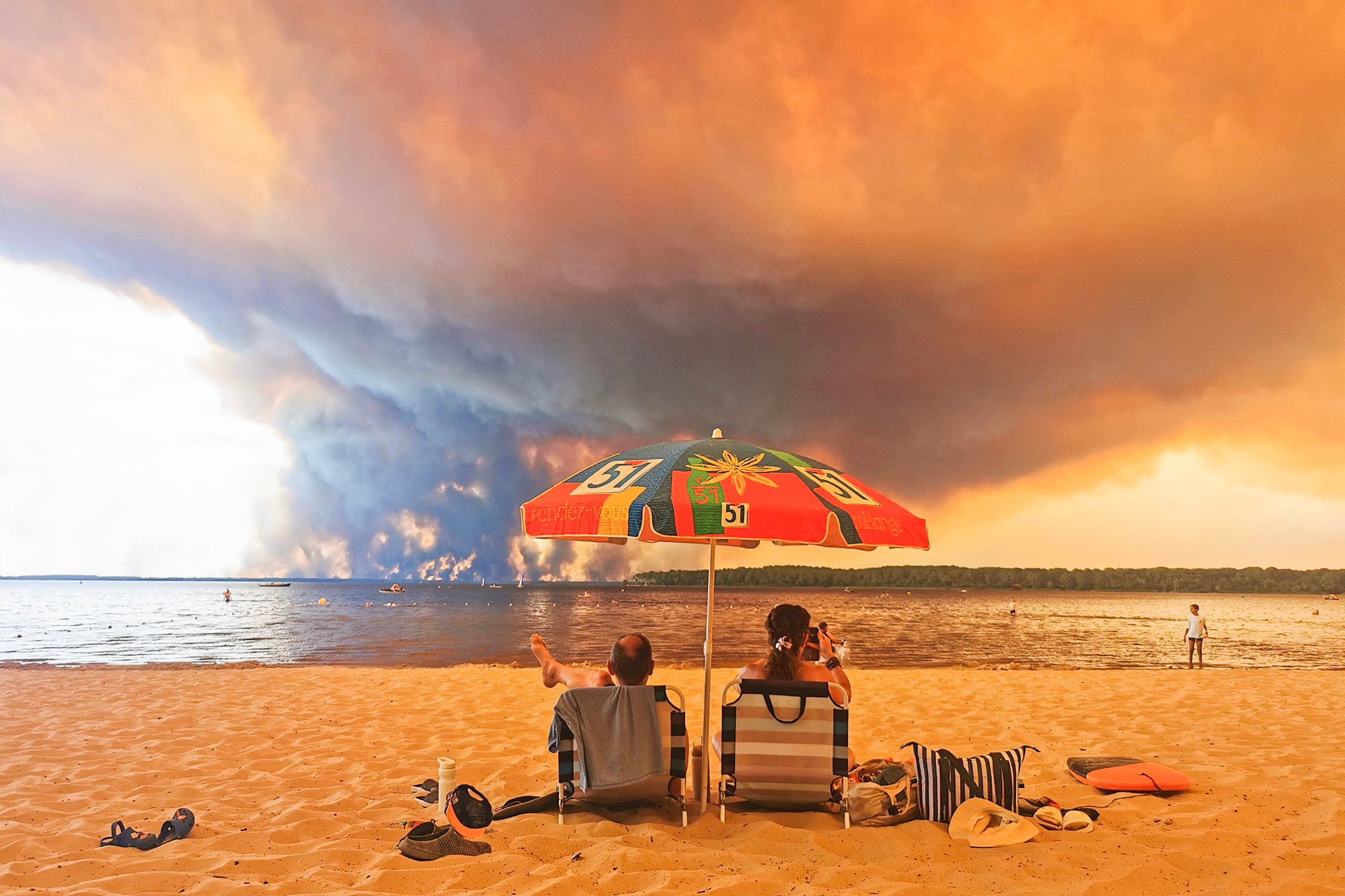Beach goers sit on the beach of Moutchic in Lacanau, southwestern France on July 24, 2026, as clouds of smoke rise into the sky from a wildfire.
