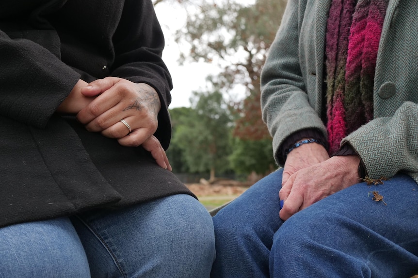 Women hold their hand in their laps while sitting in a park