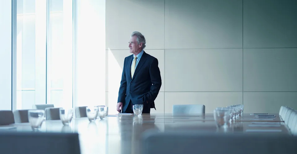 An older businessman alone in a board room, who is supposedly retired but keeps working.