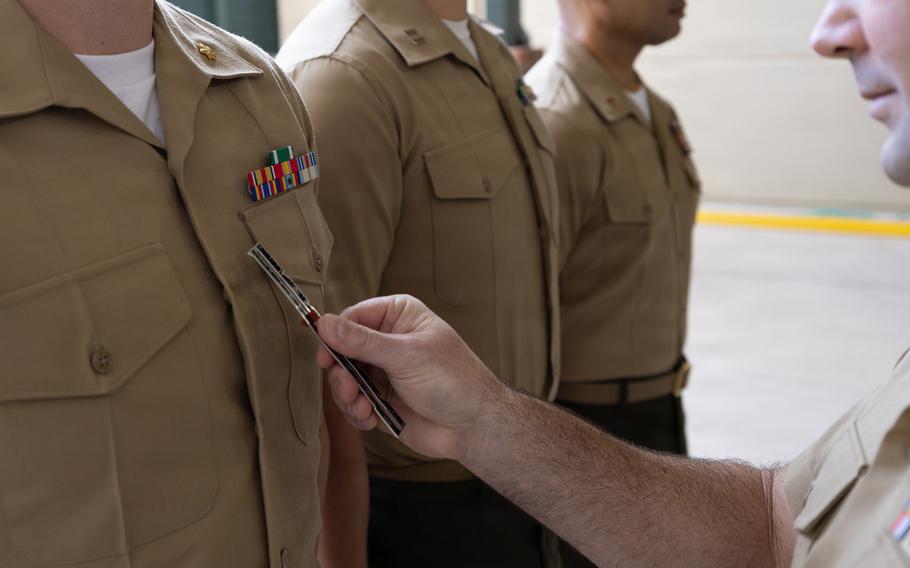 Three Marines line up as another Marine inspects their uniforms.