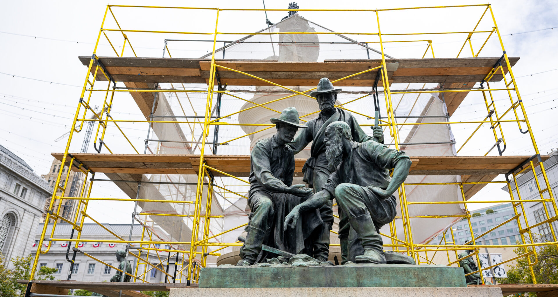 gold-covered scaffolding behind bronze statue of three miners