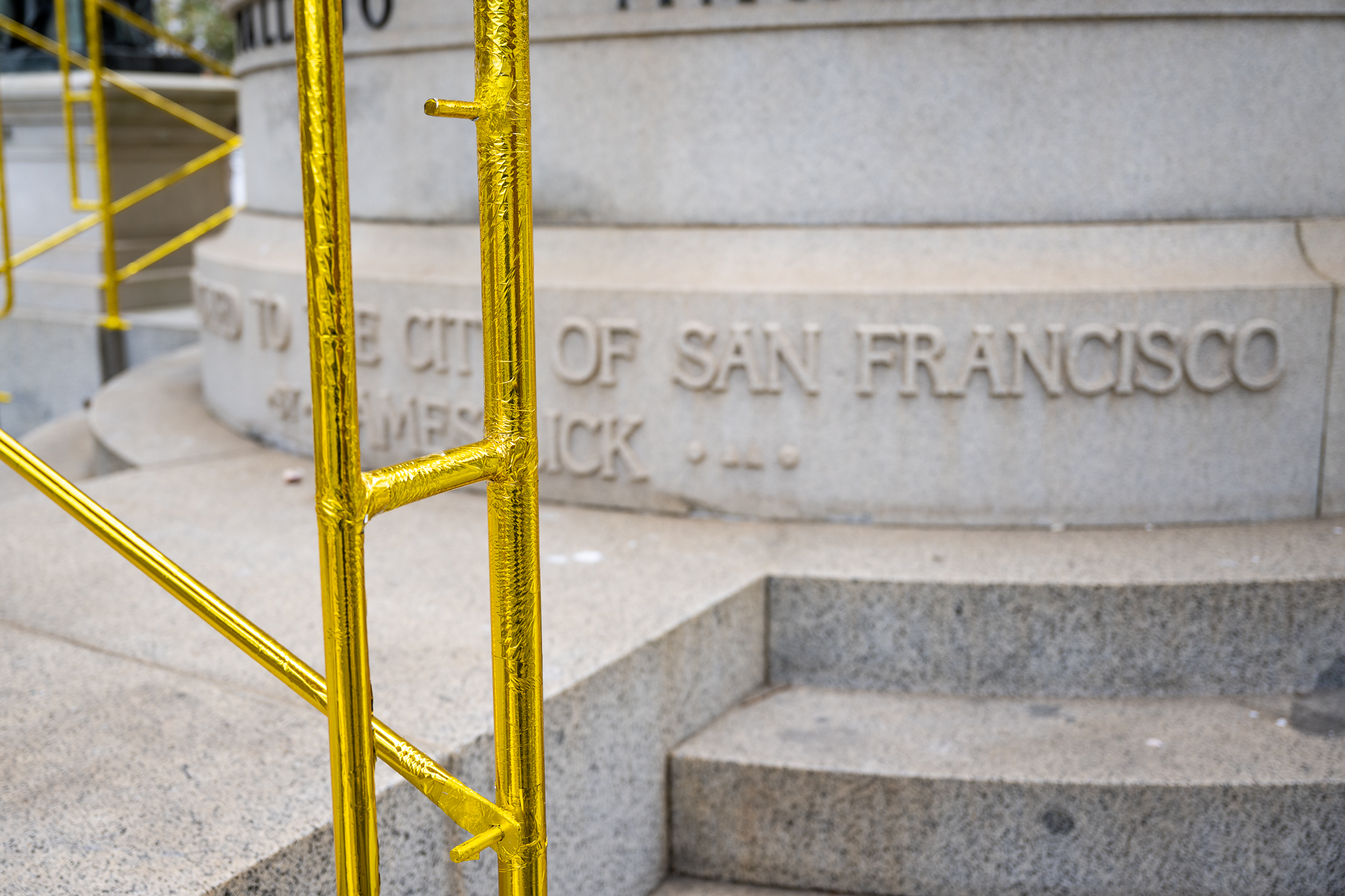 gold covered metal posts of scaffolding in front of a stone plinth