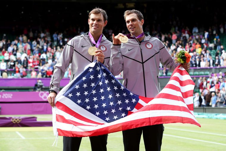 Mike Bryan, left, and Bob Bryan hold an American flag and their gold medal necklaces while posing for a photo together on the tennis court