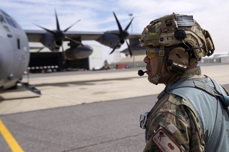 A u.s. military soldier wearing a helmet standing on a tarmac in front of a large plane.