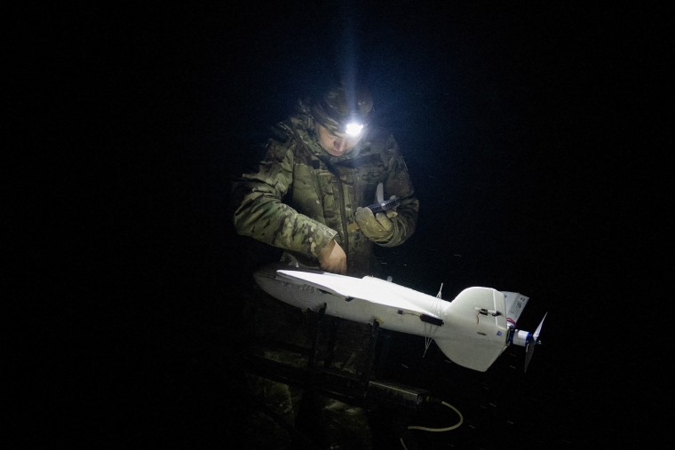 A soldier's headlamp lluminates a white, rocket-shaped device at night.