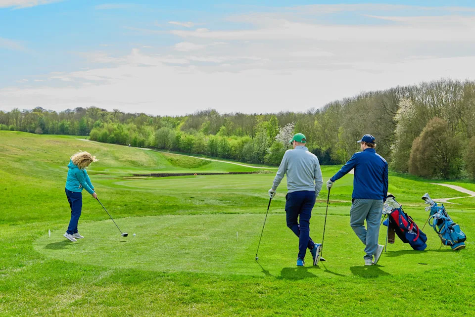 Two golfers watching another player tee off with driver