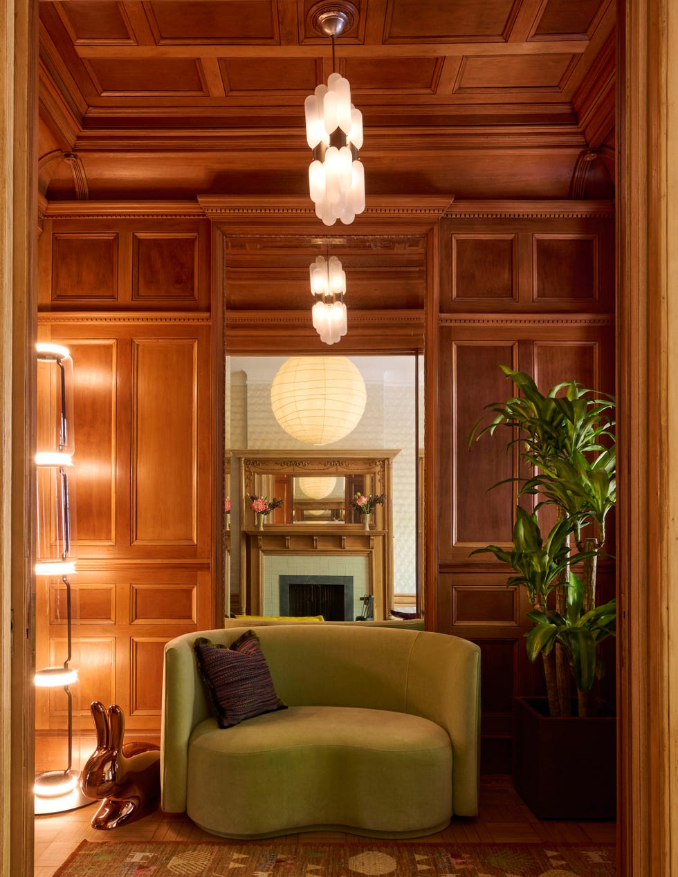Stylish interior featuring a green curved sofa, decorative lamp, and wooden paneling with a plant in a cozy setting.