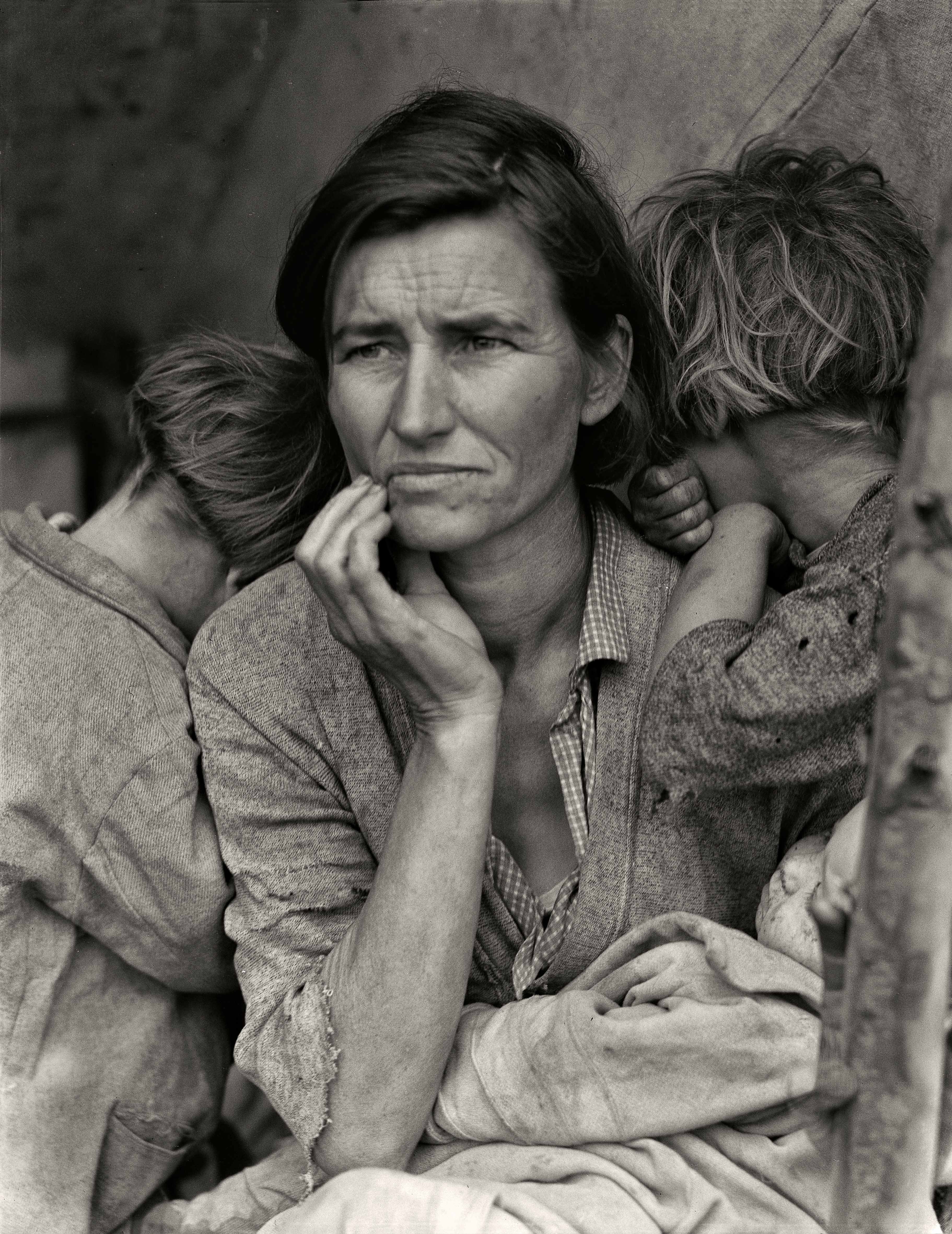 A careworn woman holds her hand to her chin while two young children press their faces against her shoulders, in Dorothea Lange's iconic 1936 portrait of a destitute pea picker in Nipomo, California.