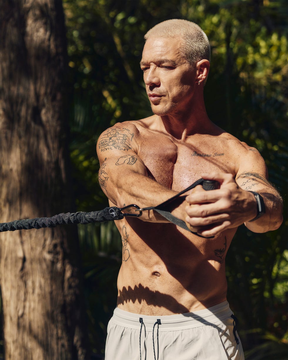 A muscular man with tattoos exercises outdoors using resistance bands. A muscular man with tattoos exercises outdoors using resistance bands.