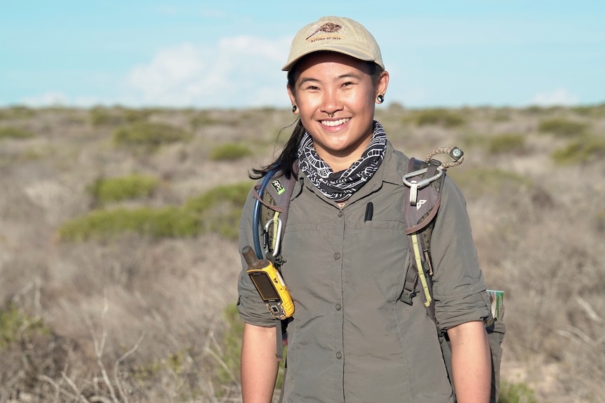 A young woman in hiking gear stands smiling on a scrubby plain.