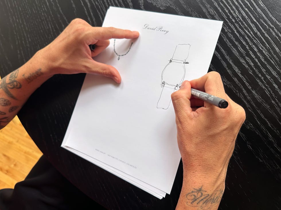 A person drawing jewelry designs on paper with a pen, showcasing a necklace and a bracelet concept sketch.