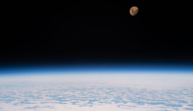 A view of the Moon from the International Space Station as it orbited 264 miles above a partly cloudy Indian Ocean southeast of Madagascar. The Moon has a golden glow to it, appearing more bronze than its usual gray. It stands out against the darkness of space, while below, Earth's atmosphere glows blue. Below that, we can see white clouds covering up most of the water below.