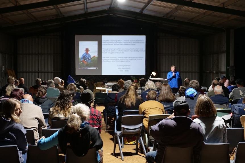 A view of people watching a movie in a large tin shed.