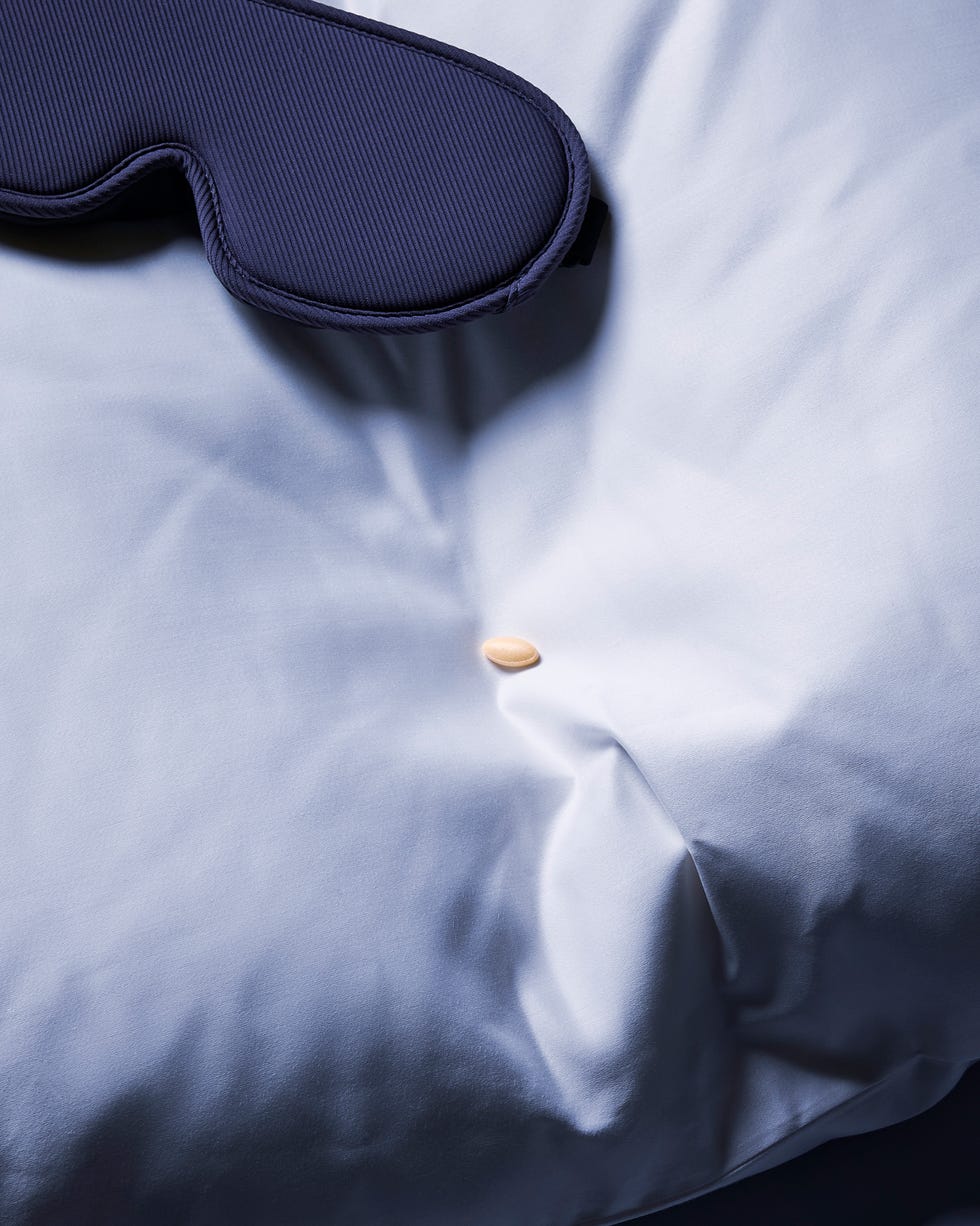 A dark sleep mask resting on a light blue pillow with a small pill nearby.