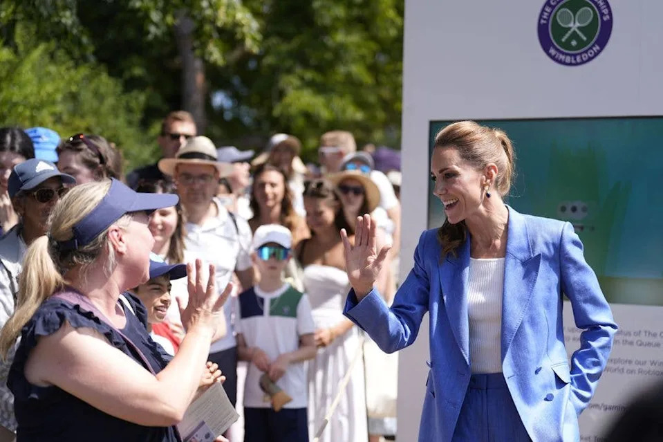 Kate Middleton in blue suit waves to woman in crowd at Wimbledon event.