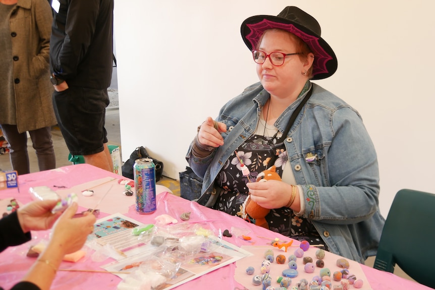 A woman sits at a table making beads out of clay.