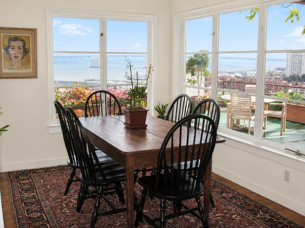 Dining room with a wooden table, black chairs, window views, and a potted plant. Dining room with a wooden table, black chairs, window views, and a potted plant.