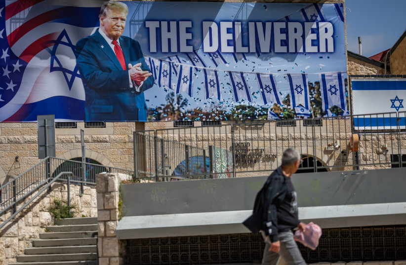Pepole walk next to a large banner depicting U.S. President Donald Trump with the slogan “The Deliverer” hangs on a building in Jerusalem, April 19, 2026.