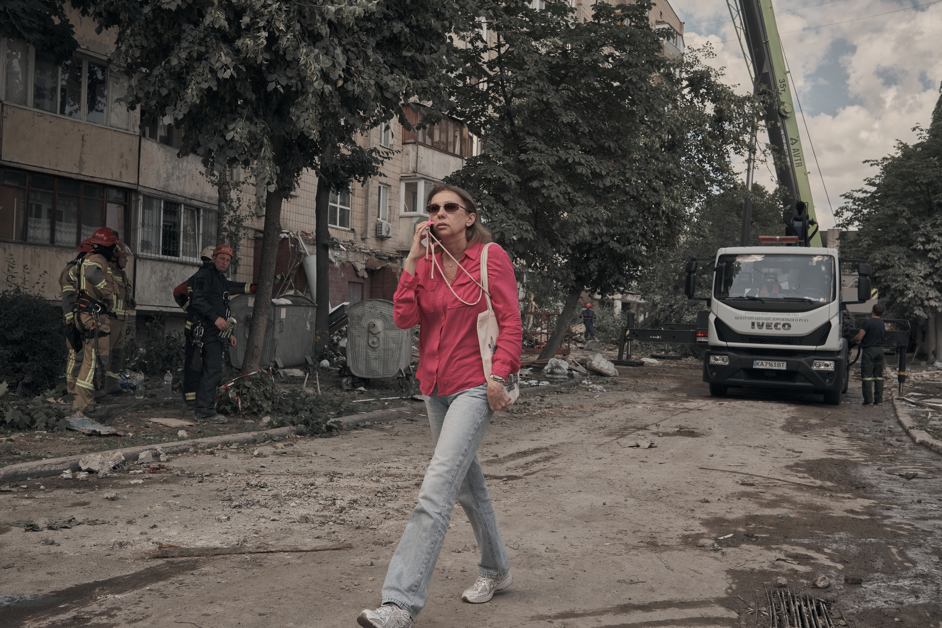 KYIV, UKRAINE - JULY 06: A woman on her mobile phone walks past rescuers working at a nine-story residential building in Kyiv's Podilskyi district after a Russian missile strike destroyed floors from the fifth to the ninth on July 6, 2026 in Kyiv, Ukraine. Kyiv endured a massive Russian missile and ballistic attack, with at least 24 people reported injured and the death toll rising to seven after rescuers recovered two more bodies from under the rubble, according to Tymur Tkachenko, head of the Kyiv City Military Administration. Ukraine's State Emergency Service worked to extinguish the fire and clear debris as they searched for and worked to free people trapped under the rubble. Seventeen people were brought out into fresh air, while another 28 were rescued from the upper floors with the help of an aerial ladder, as search operations continued. (Photo by Kostiantyn Liberov/Libkos/Getty Images)