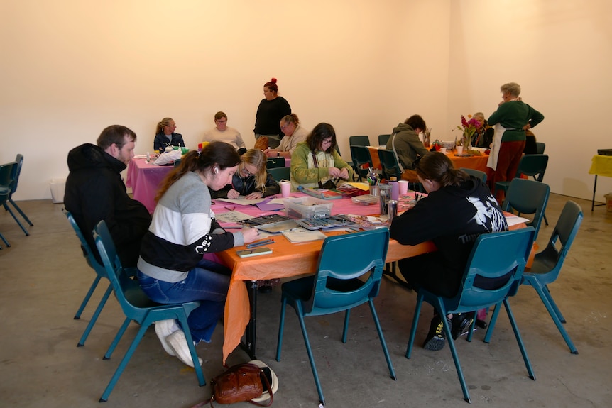 A group people sit at tables drawing and colouring in.