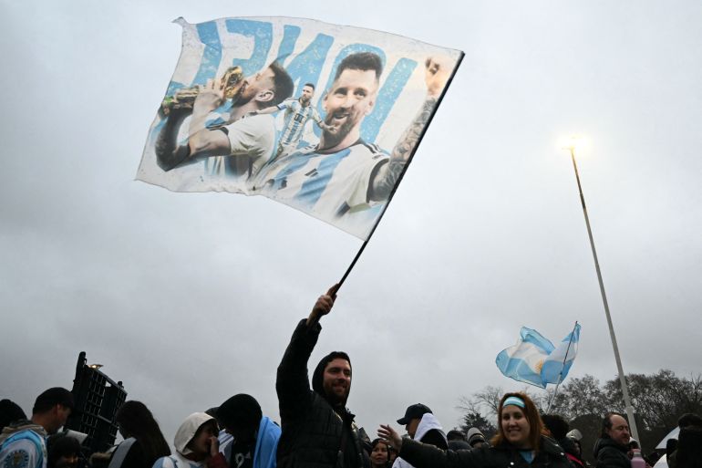 A fan waves a flag bearing images of Argentina's forward Lionel Messi near the Argentine Football Association (AFA) training camp in Ezeiza, Buenos Aires Province, on July 20, 2026, while waiting for the arrival of Argentina's national football team from the United States following its defeat in the 2026 FIFA World Cup final. (Photo by Luis ROBAYO / AFP)
