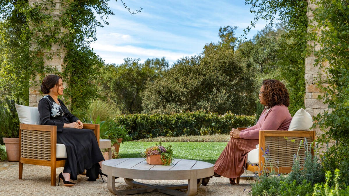 Meghan Markle in a dark black dress sitting opposite from Oprah Winfrey in California.