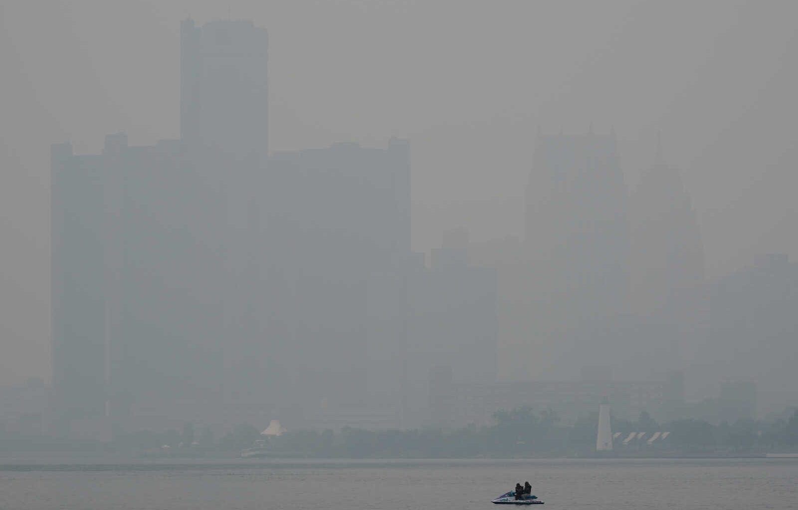 Hazy city skyline across a calm river; a small motorboat with two people in the foreground.