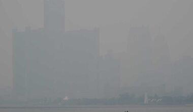 Hazy city skyline across a calm river; a small motorboat with two people in the foreground.