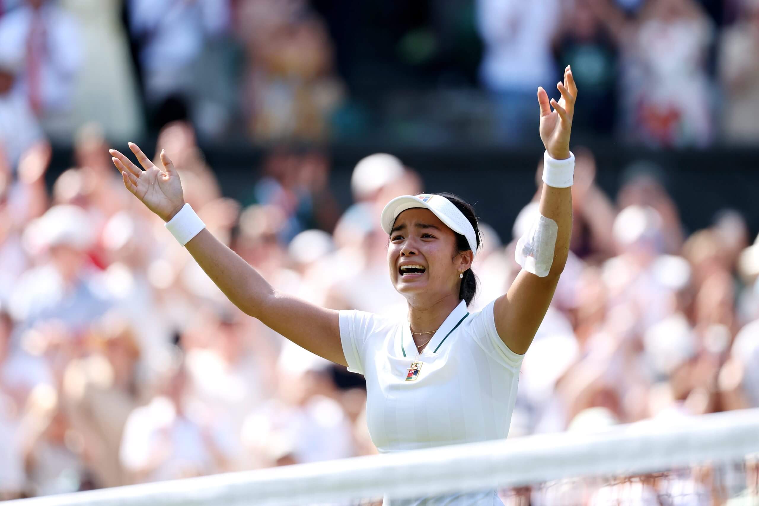 Alex Eala raises her arms in celebration in front of a crowd in soft focus.