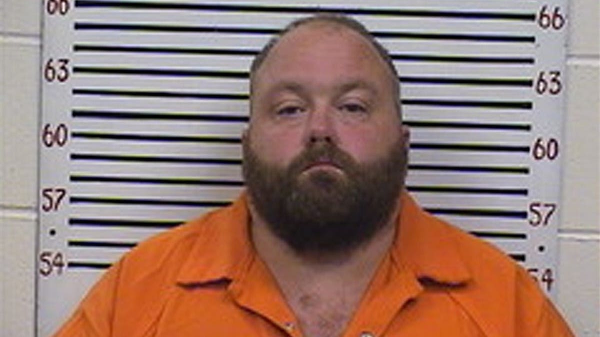 Booking photo of George Birmingham, a bearded man in an orange jail uniform, standing in front of a height-measurement wall.