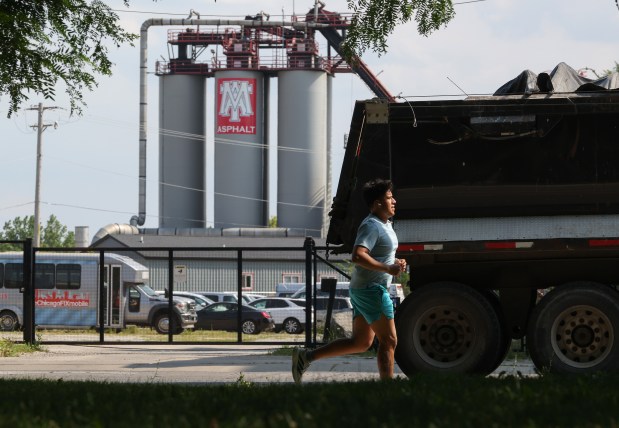 An asphalt truck passes a jogger running along the south end of McKinley Park, across the street from MAT Asphalt in the 2000 block of West Pershing Road on July 23, 2026, in Chicago. (John J. Kim/Chicago Tribune)
