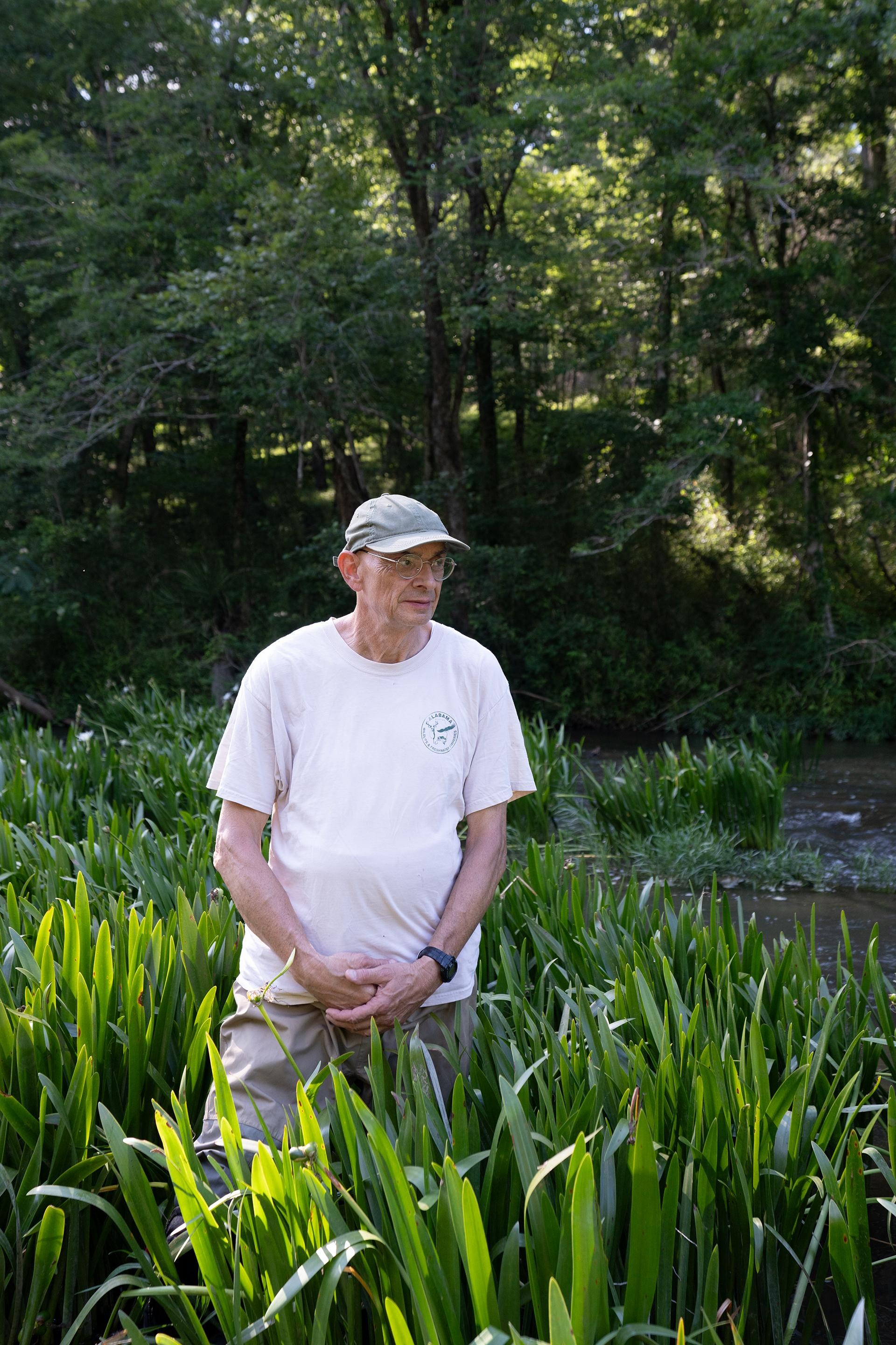 Paul Johnson stands in a marshy area, with a light-colored T-shirt and baseball cap.