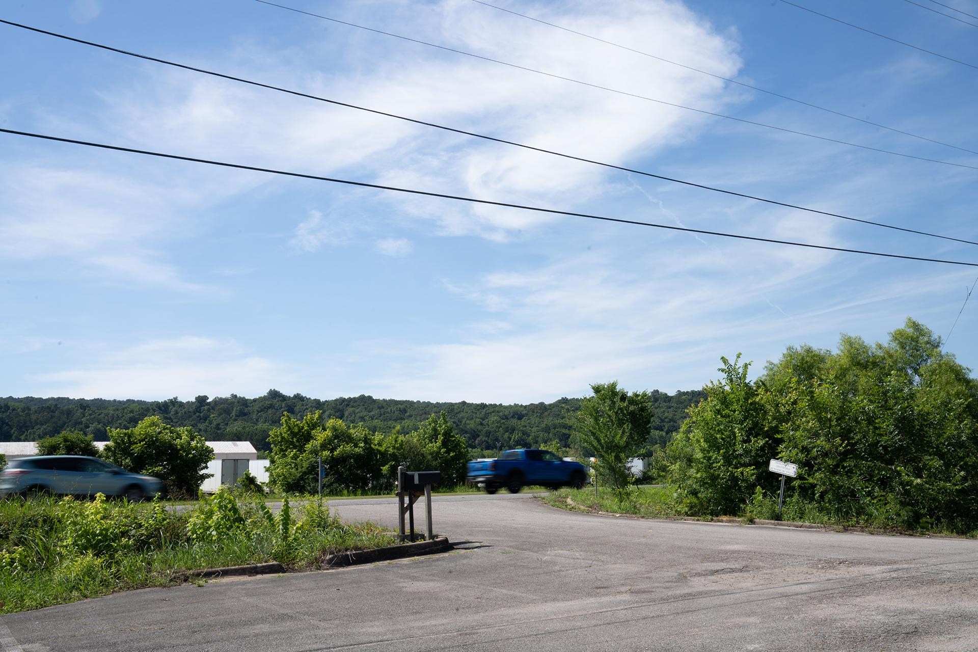 A stream runs between a highway and a parking lot, with cars driving by.