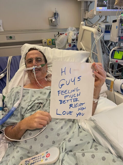 peterson holds sign up in hospital bed that reads "hi guys feeling much better right now love you"