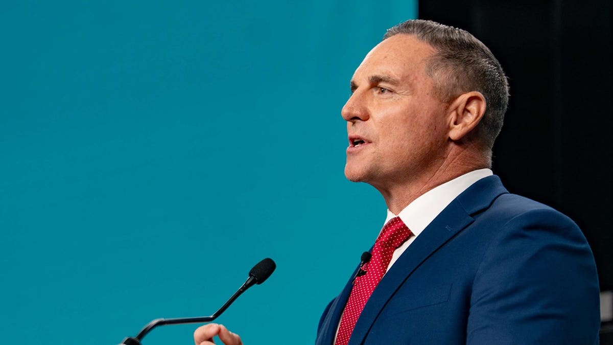 Jay Feely stands at a debate podium in a studio.