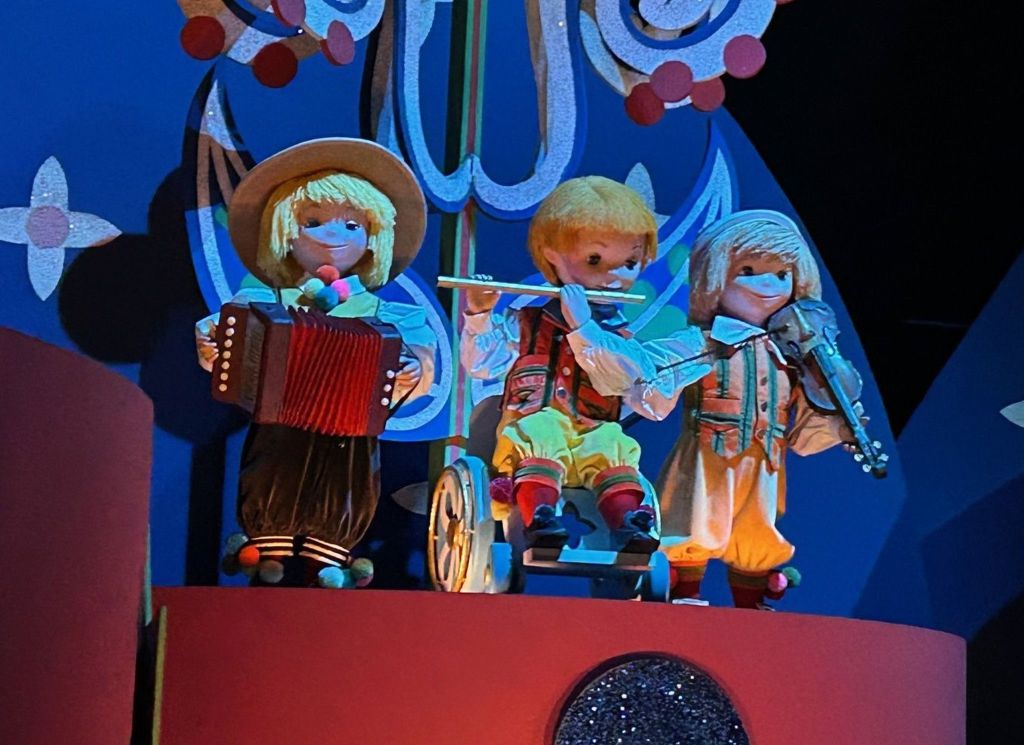 Three animatronic dolls playing musical instruments on a stage.