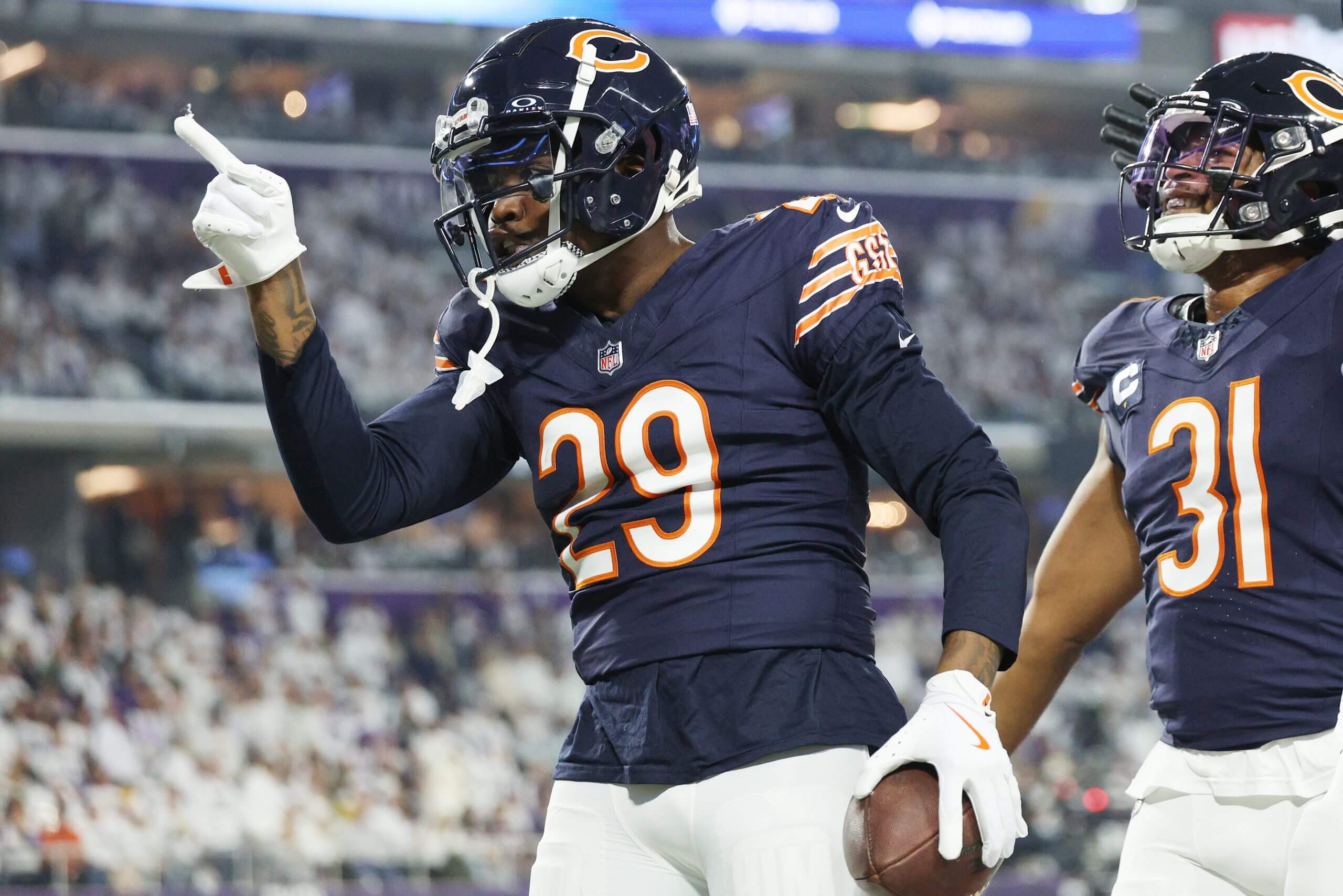 Chicago Bears cornerback holds the football with his left hand and points ahead with his right index finger during an NFL game.