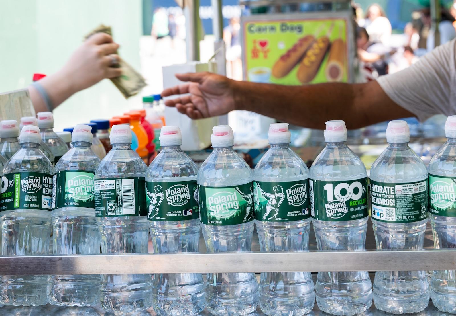 a customer pays a street food vendor cash. bottles of water and sports drinks line the food cart