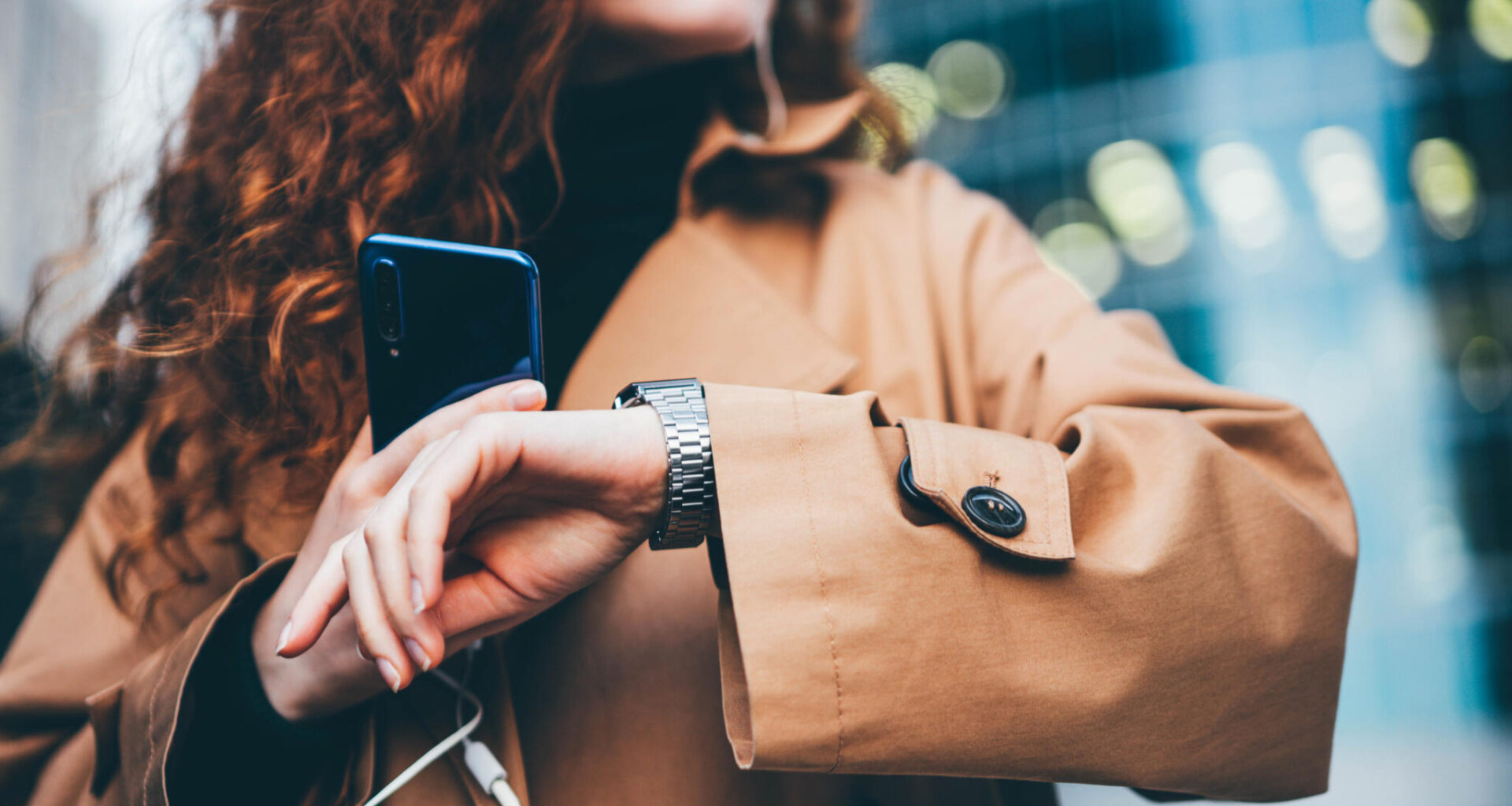 A woman checks her watch while holding a smartphone. (Maria Korneeva/Getty Images)