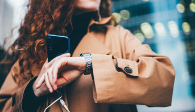 A woman checks her watch while holding a smartphone. (Maria Korneeva/Getty Images)