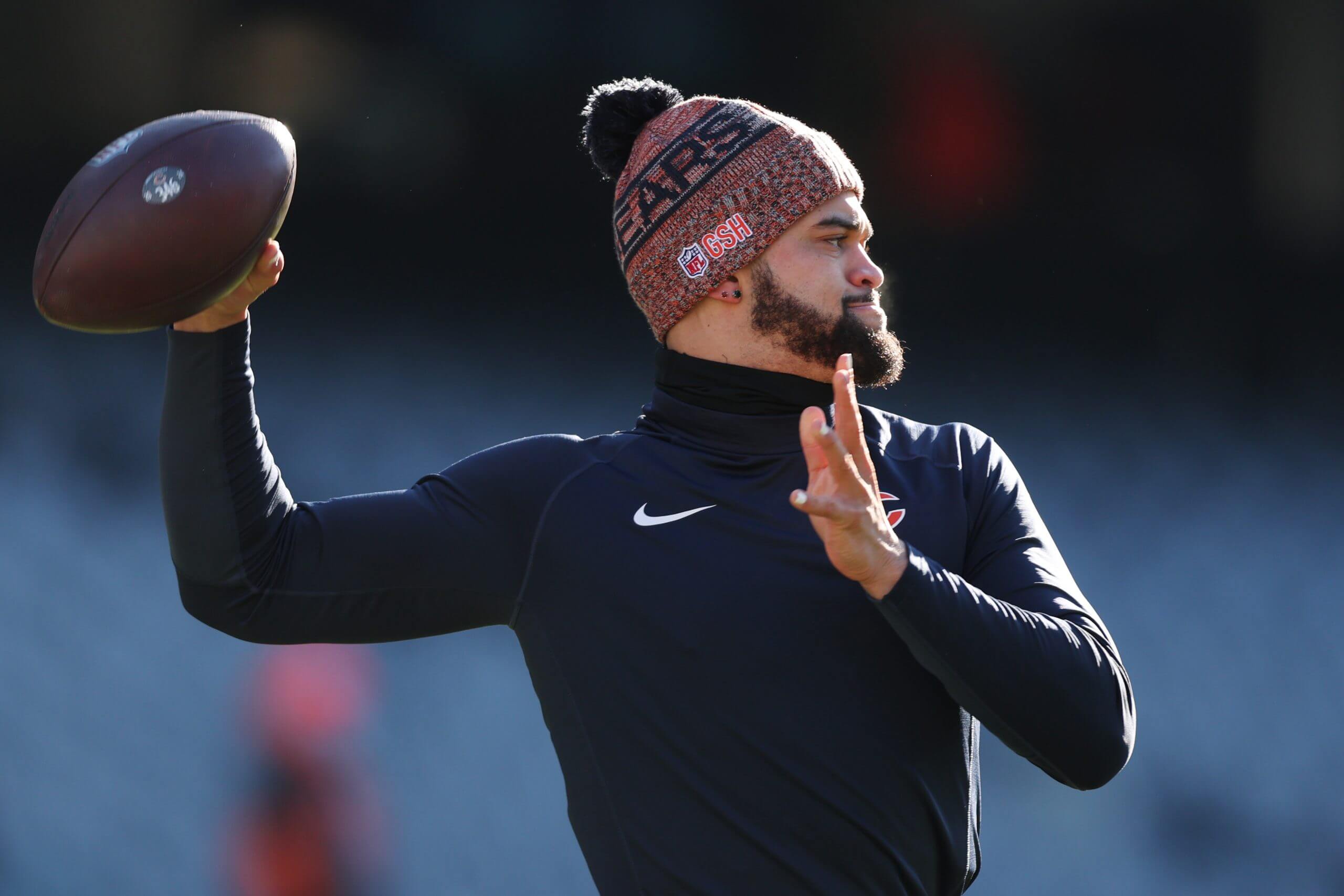 Chicago Bears quarterback, wearing an orange-and-black knit cap, prepares to throw the football while warming up for an NFL game.